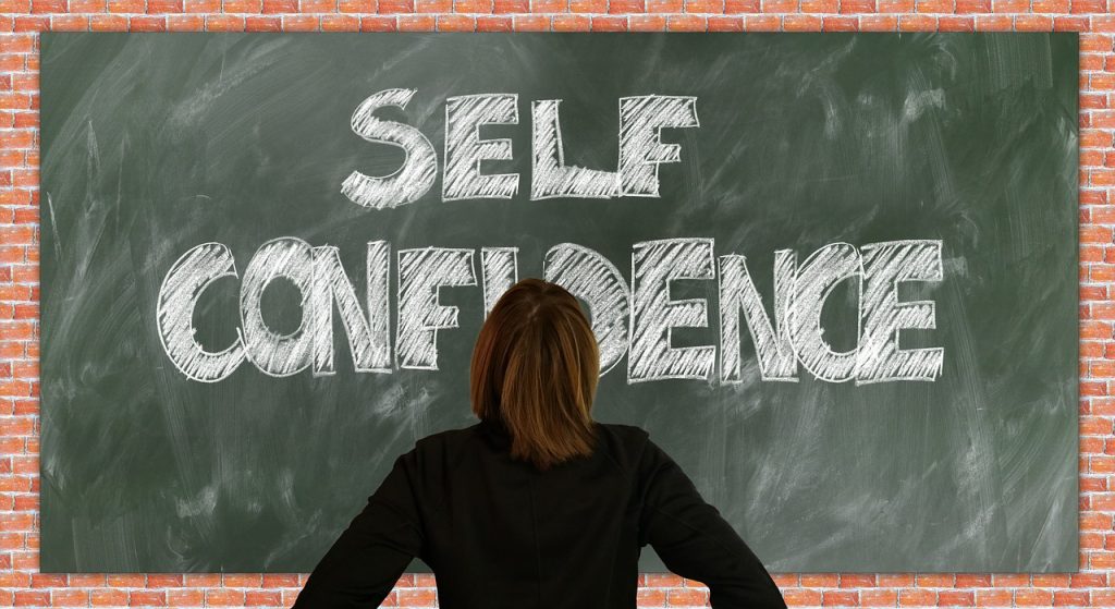 A woman looking at the board saying 'Self Confidence'